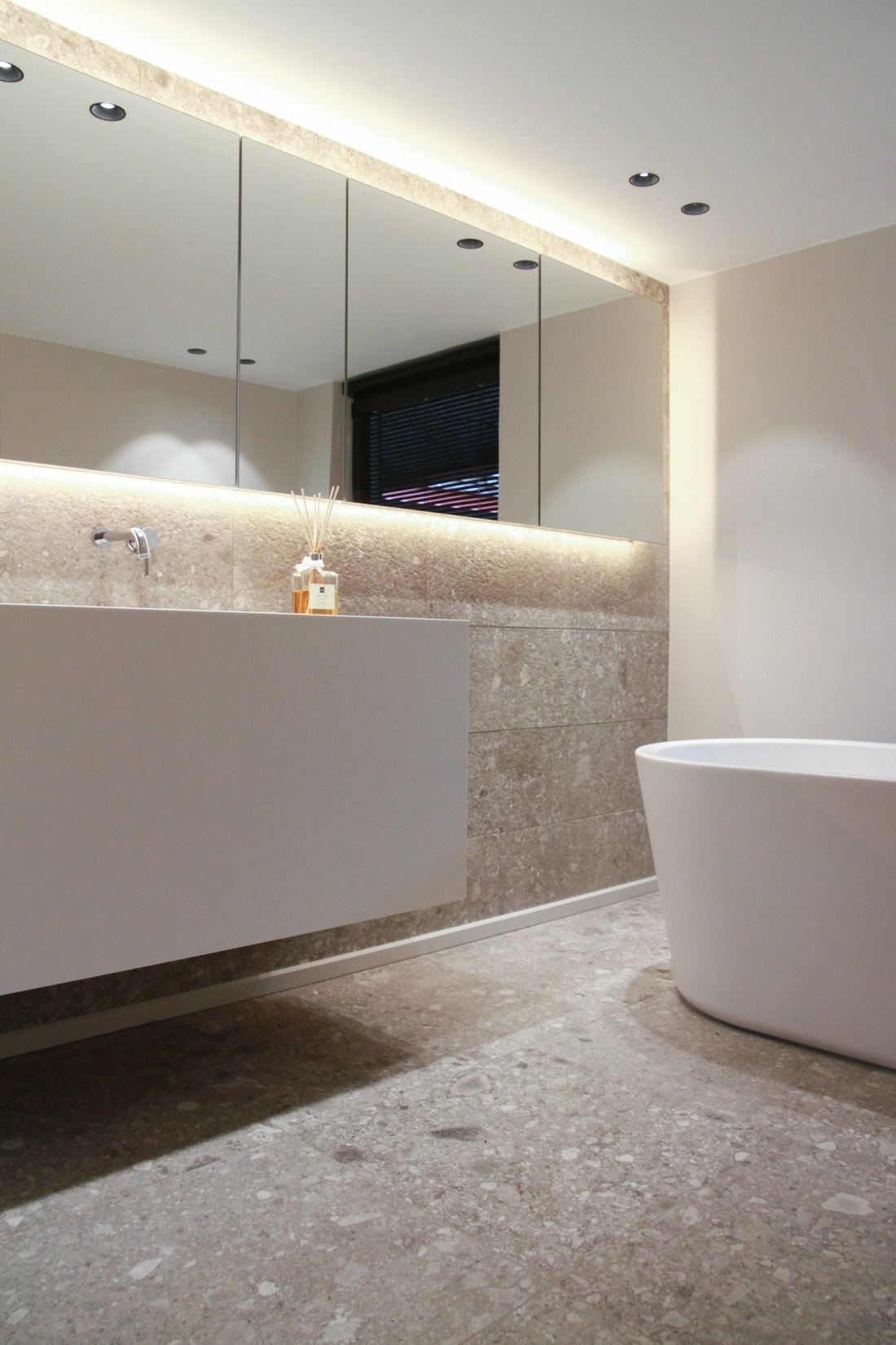 Calm, minimal bathroom in warm cream tones with a freestanding bath