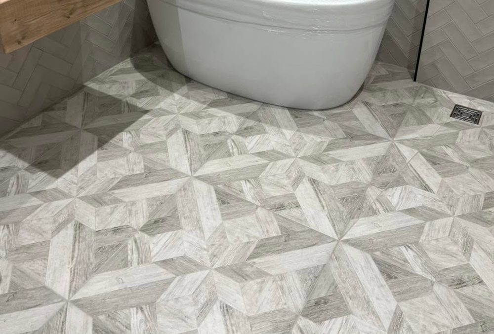 Freestanding bath on patterned grey floor tiles with herringbone wall tiling behind