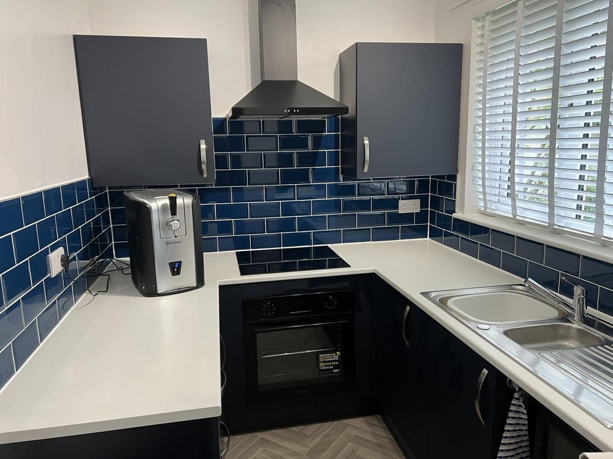Kitchen with deep blue metro tile splashback, white worktops and dark grey cabinets