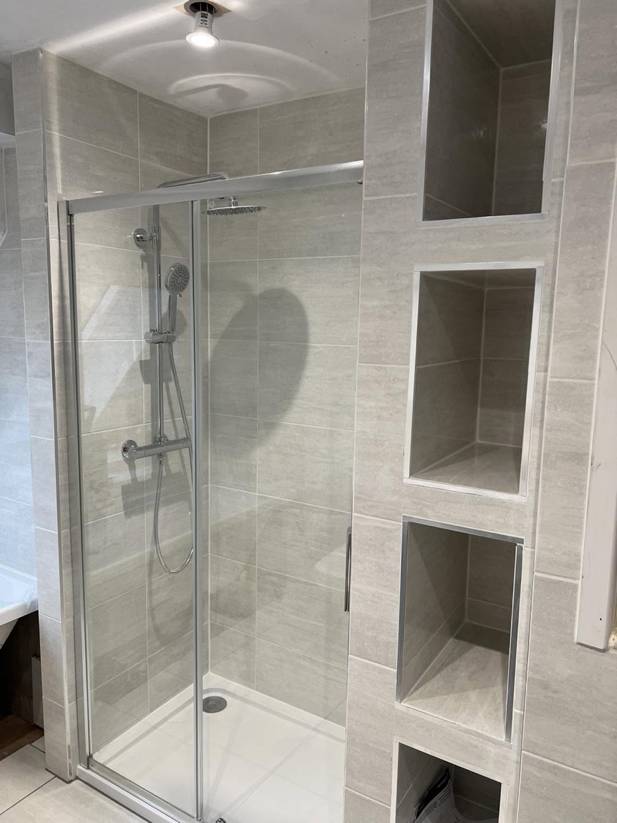 Finished walk-in shower with sliding glass door, rainfall shower head and four tiled storage niches